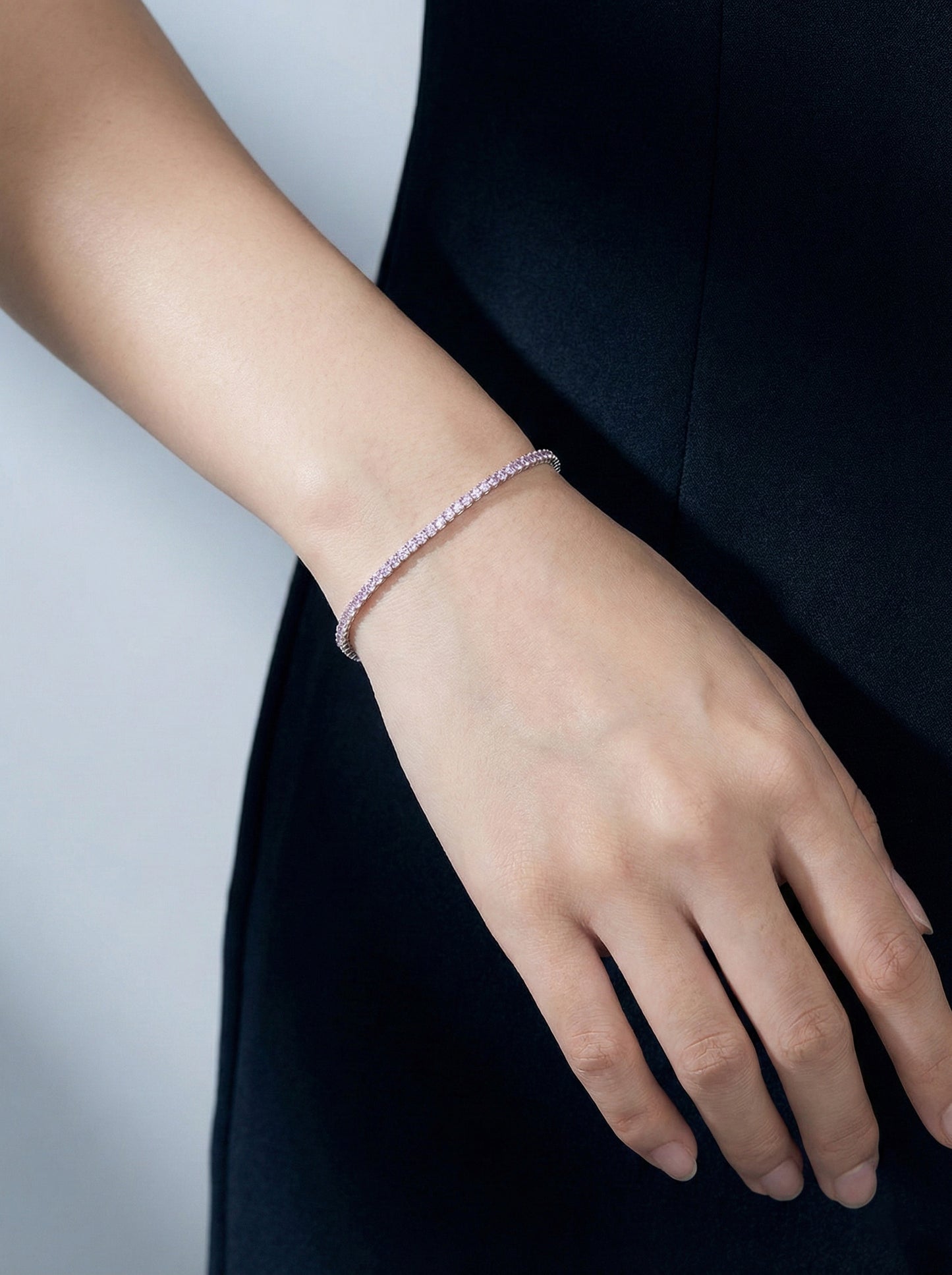 Model’s arm styled with the dainty 925 silver Amore tennis bracelet, featuring a continuous row of sparkling pink stones, paired with a pink top and blue jeans for a playful everyday look.