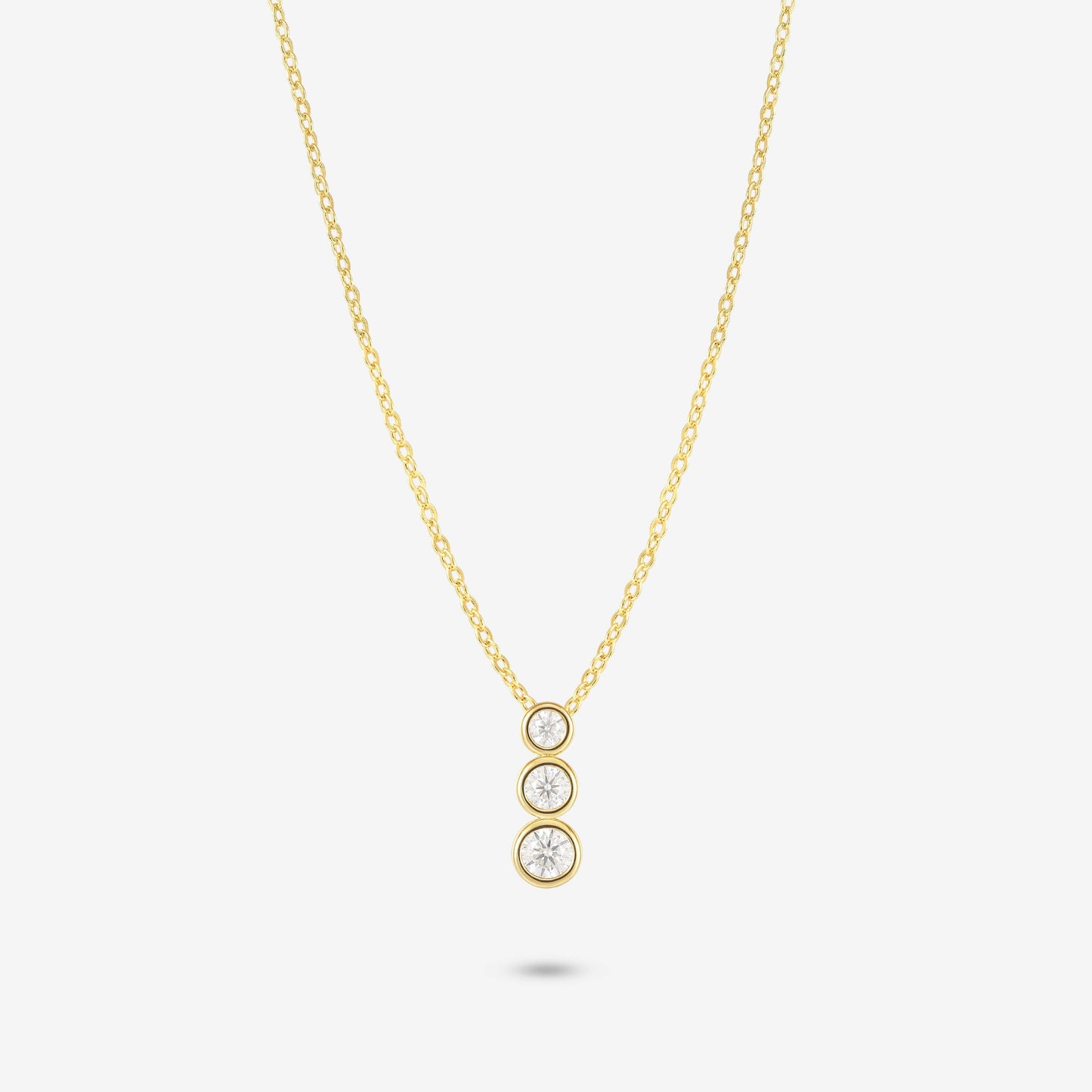 Studio shot of the Gold Aviel Necklace featuring three round bezel-set moissanite stones in a vertical drop, on a light grey background
