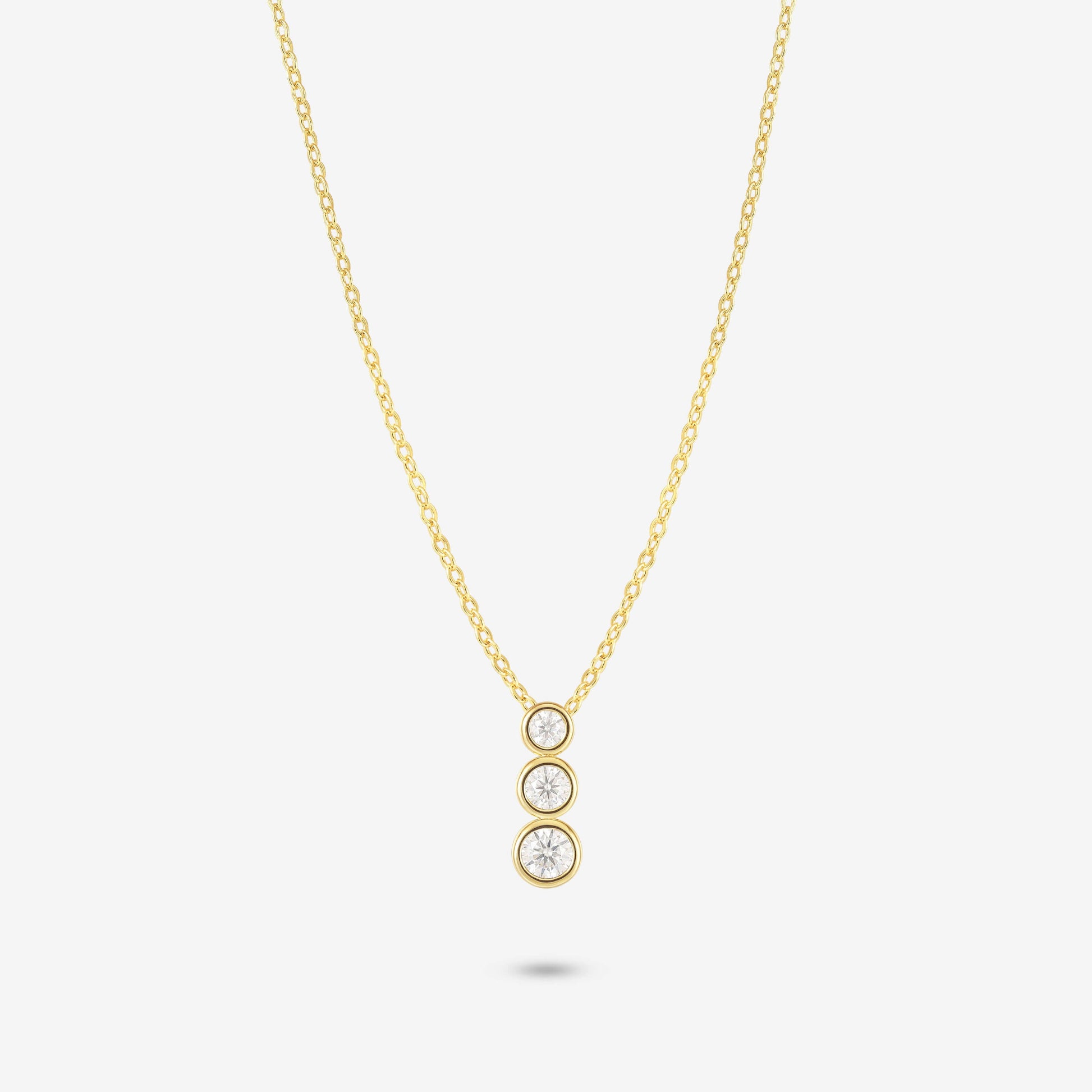 Studio shot of the Gold Aviel Necklace featuring three round bezel-set moissanite stones in a vertical drop, on a light grey background