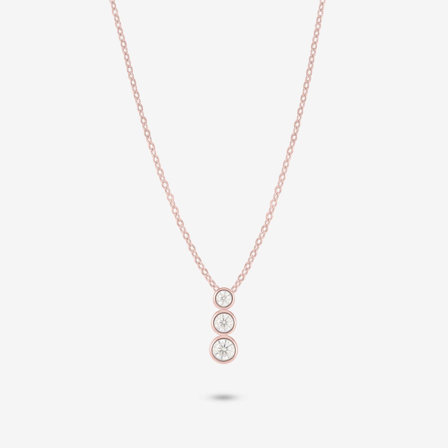 Studio shot of the Rose Gold Aviel Necklace with three graduated bezel-set moissanite stones in a pendant, photographed against a neutral grey backdrop