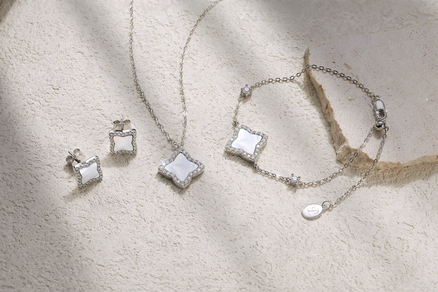 Elegant flat lay of the Pure Moments Edea quatrefoil jewellery set featuring matching necklace, bracelet, and stud earrings in rhodium-plated 925 silver with mother of pearl and pavé moissanite accents.