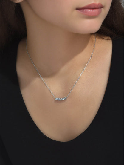 Model wearing the chic 925 Silver Dawn Necklace with a fine chain and horizontal bar pendant featuring five round bezel-set sparkling stones, styled over a cream satin top.