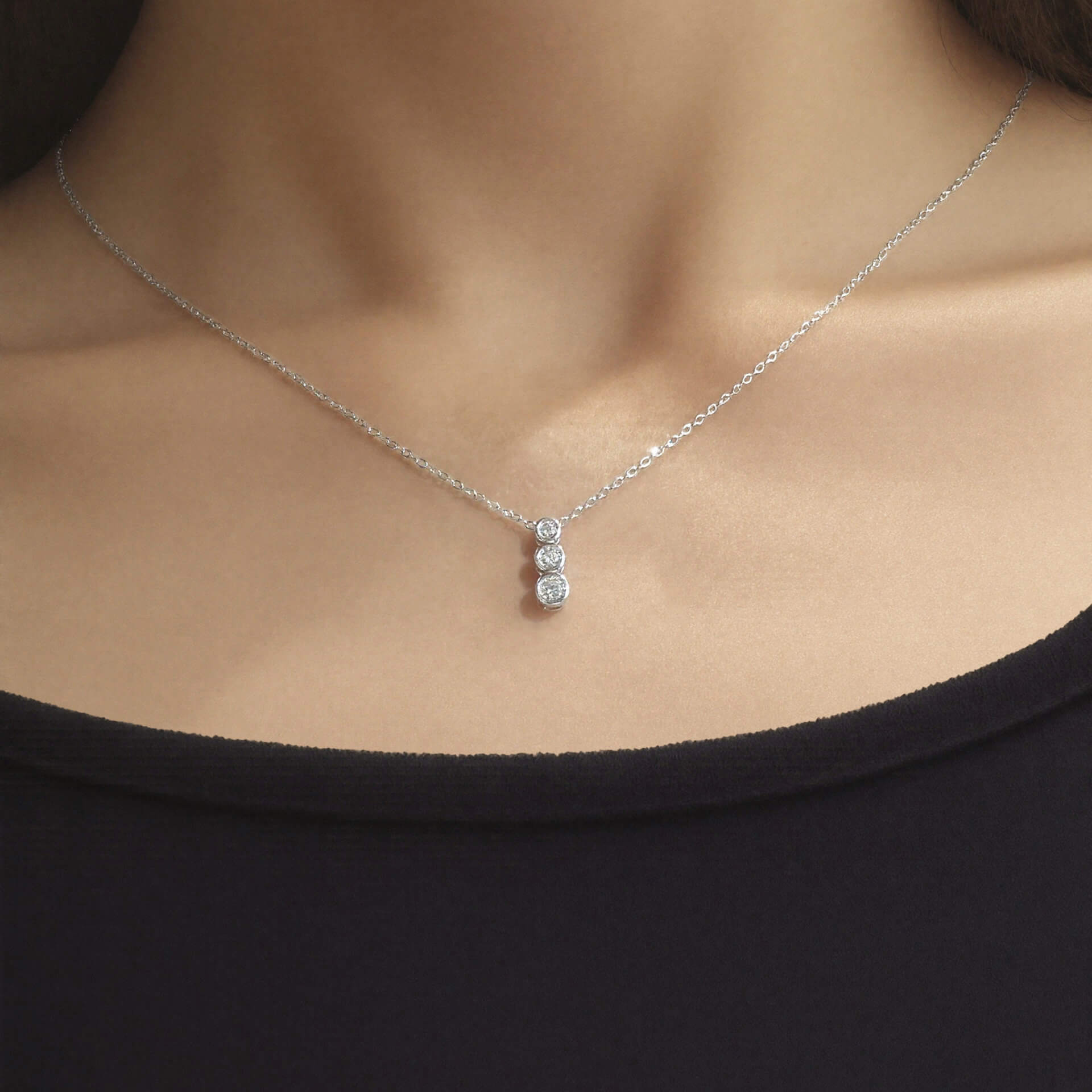 Model wearing the elegant 925 Silver Aviel Necklace, featuring a fine chain and a vertical pendant with three round bezel-set sparkling stones, styled over a white top.