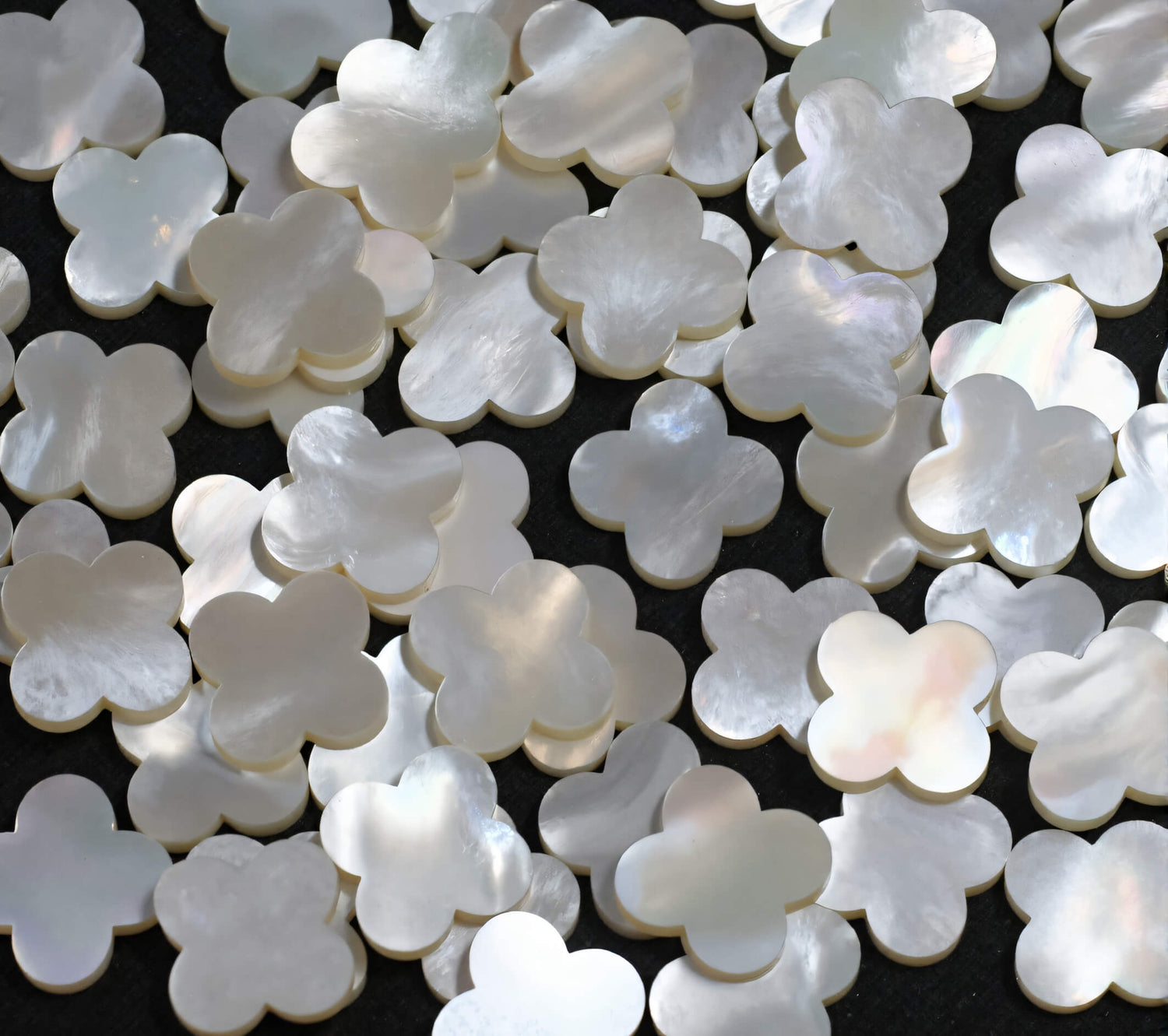 A macro shot of lustrous, iridescent Mother of Pearl charms carved in a classic quatrefoil shape, the heart of our elegant jewellery collection.
