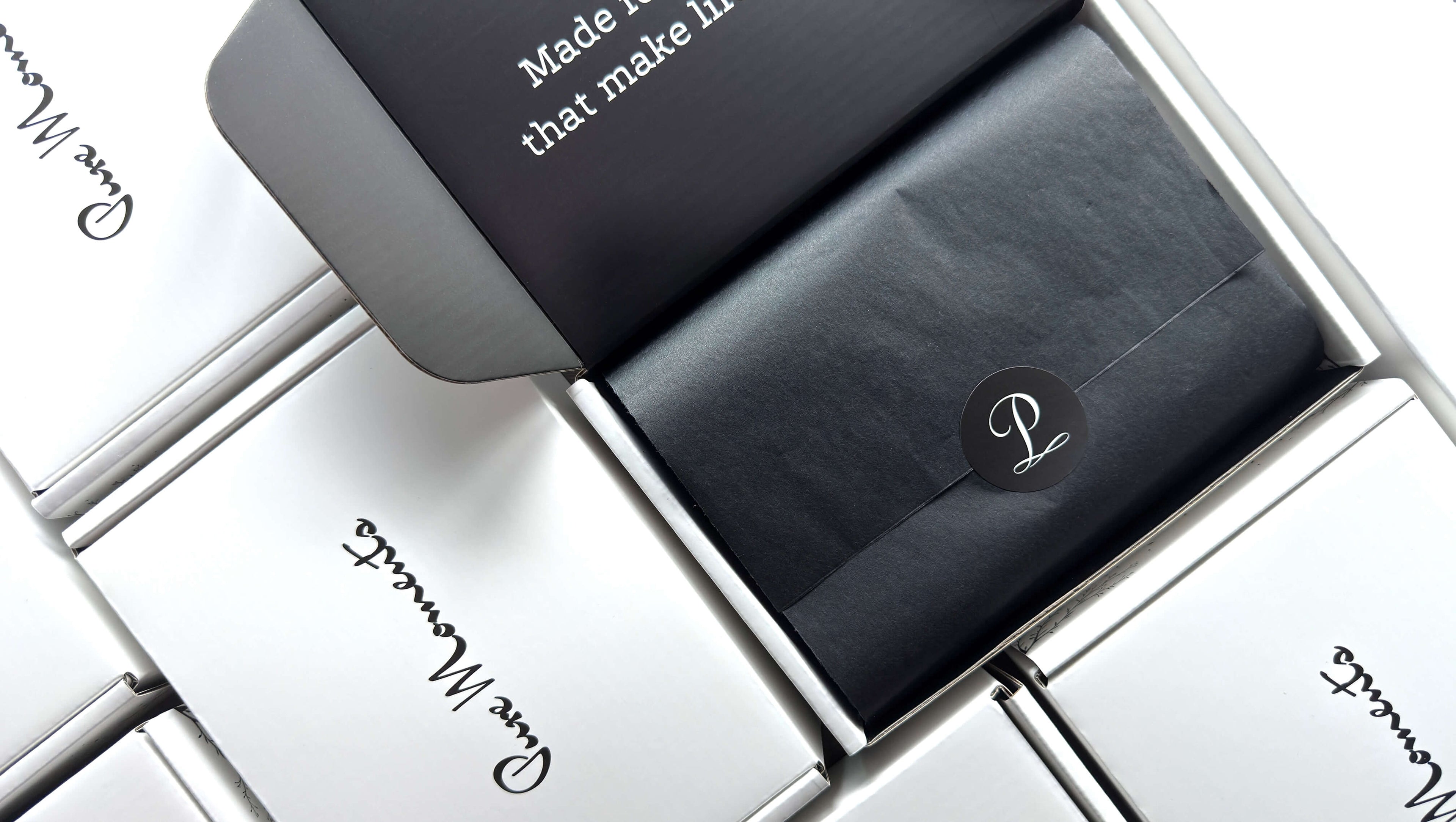 An open white Pure Moments shipping box revealing black tissue paper with a logo sticker, surrounded by other closed boxes, showcasing our signature packaging.