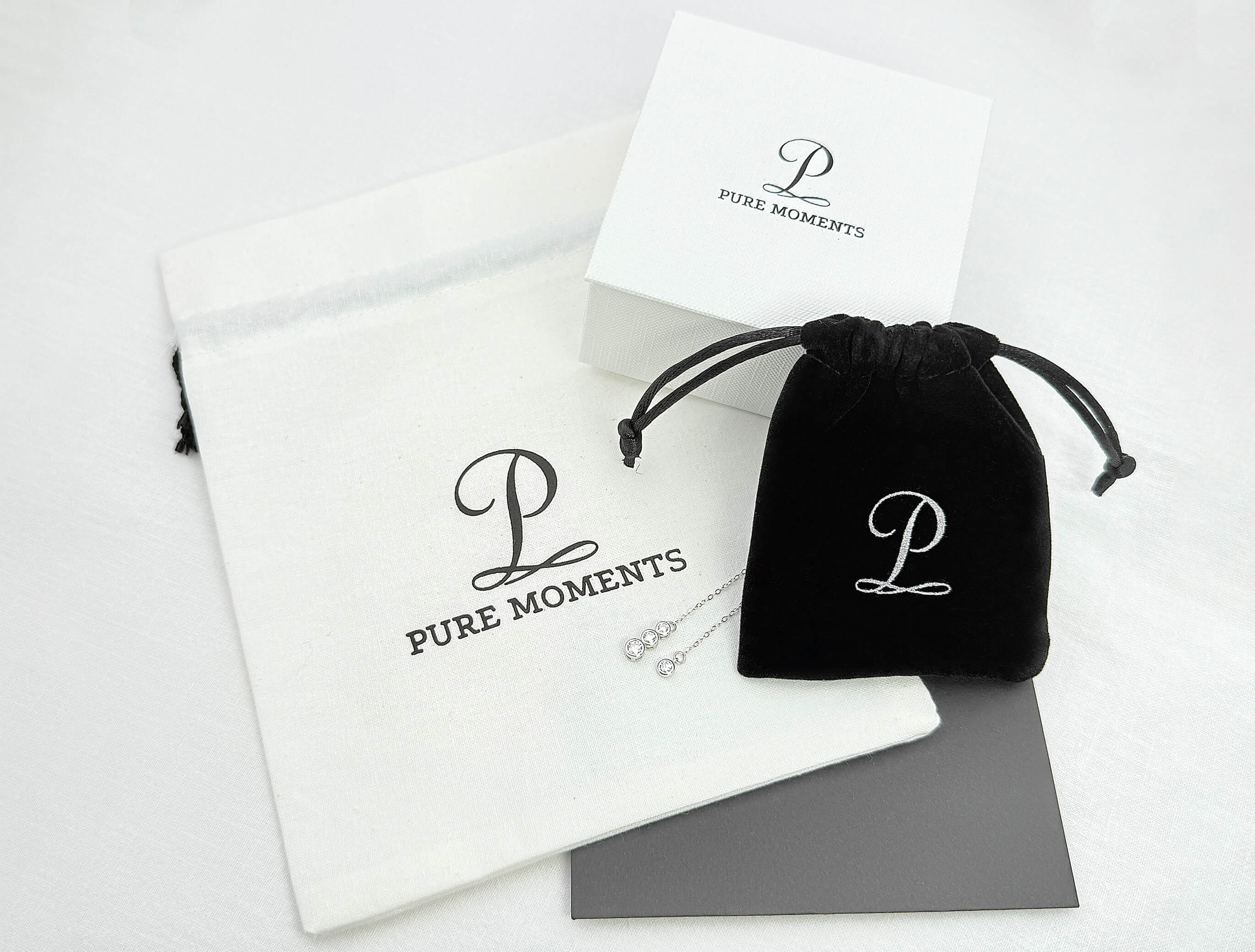 The complete Pure Moments signature packaging suite, featuring our elegant white jewellery gift box, soft black velvet pouch, white cotton drawstring bag, and polishing cloth for your jewellery.