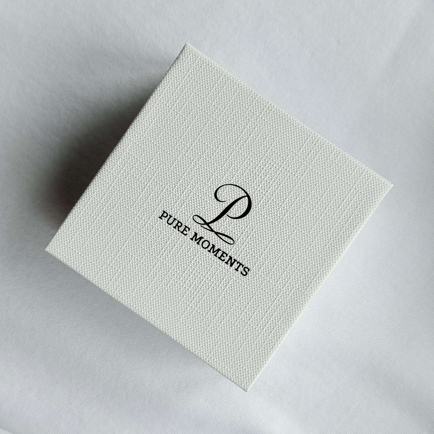 Pure Moments jewellery gift box with a white textured finish and black logo, viewed from above, showcasing our signature minimalist packaging.