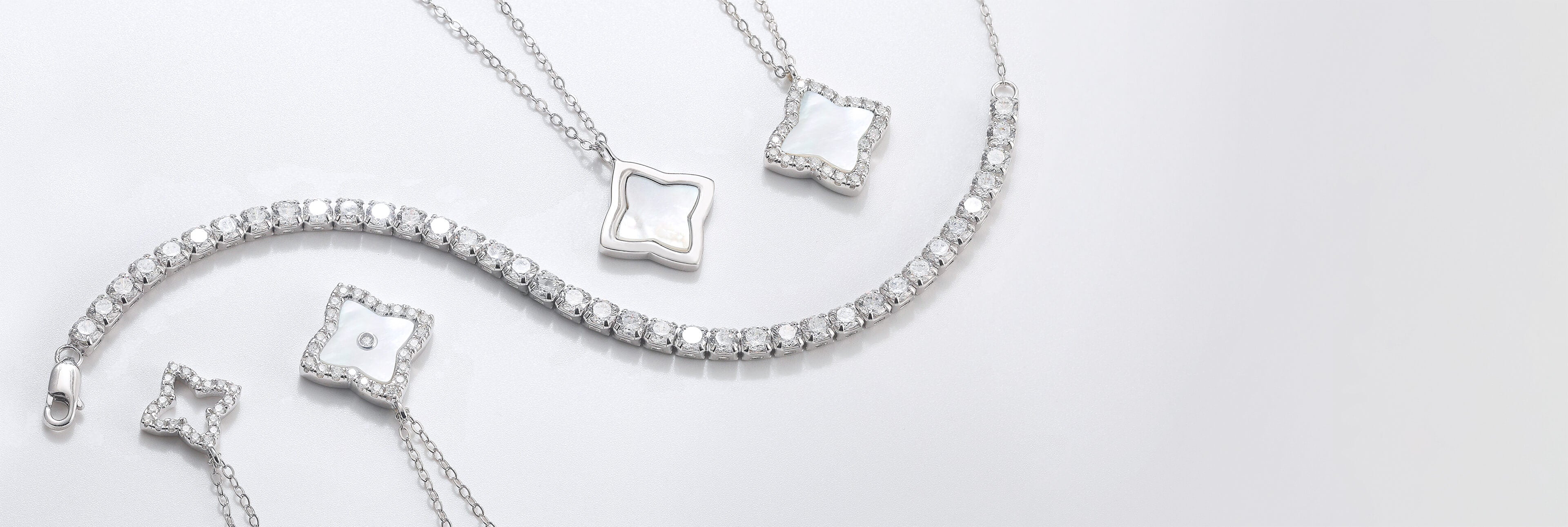 A flat lay of the "Chapter 0: Origin" collection, featuring our quatrefoil motif jewellery in 925 silver and mother of pearl with sparkling moissanite pavé accents, displayed alongside our classic tennis bracelet.