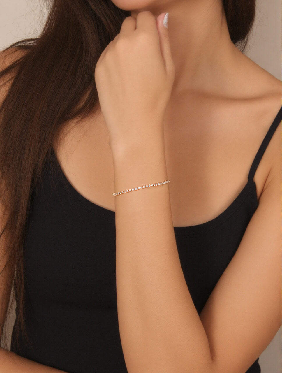 Model’s wrist adorned with a warm-toned 18k rose gold tennis bracelet featuring lustrous stones, styled against a dark top for a modern, elegant look.